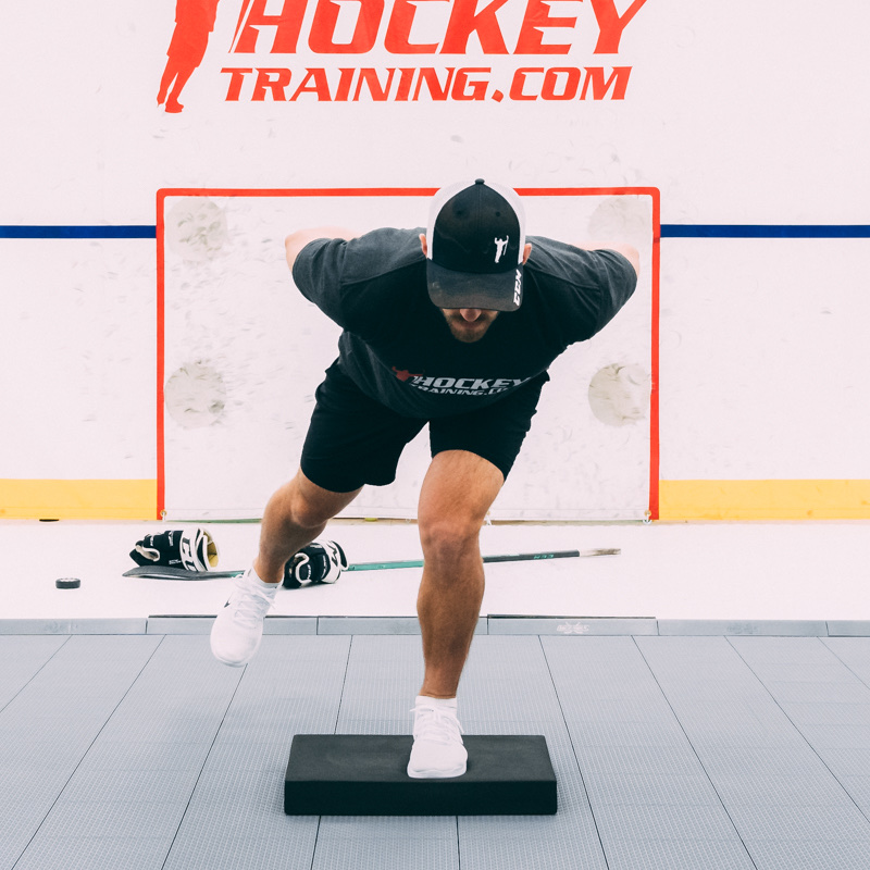 Coach Kevin balancing on one leg on a foam pad.